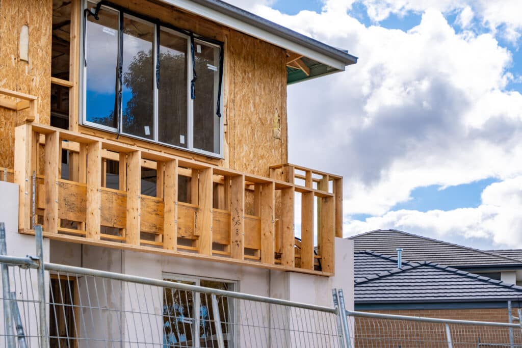Raw construction phase of a residential building, the framework of a balcony and upper-level extension of a two-story house. Exposed timber beams and unfinished surfaces of a future suburban home