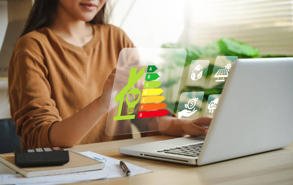 Femme interagit avec une interface holographique affichant l'efficacité énergétique (A-G) d'une maison. Icônes de durabilité, solaire, économie verte et empreinte carbone.